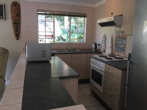 A kitchen with a stove, sink, and window. - Six on Green Cottage (Johannesburg)