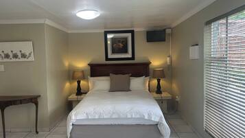 A bedroom with a bed, bedside lamps, a nightstand, a bench, a framed picture, a ceiling light, and a window with blinds.