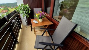 A balcony with a wooden table, two chairs, a potted plant, and a vase of flowers.
