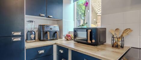 A modern kitchen with blue cabinets, a coffee maker, a microwave, and wooden utensils on the counter.
