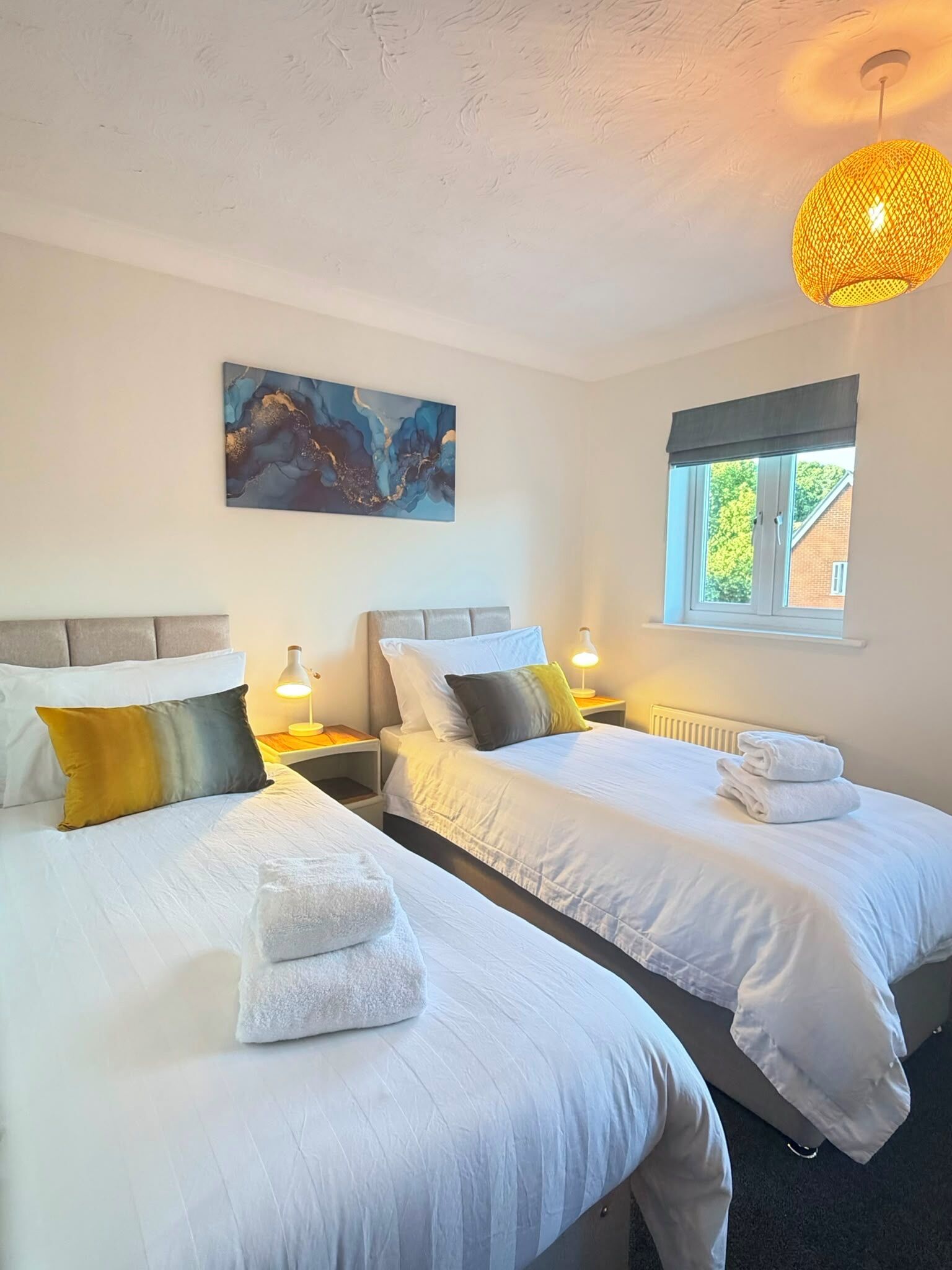 Een hotelkamer met twee bedden, een schilderij aan de muur, een raam met uitzicht en een hanglamp.