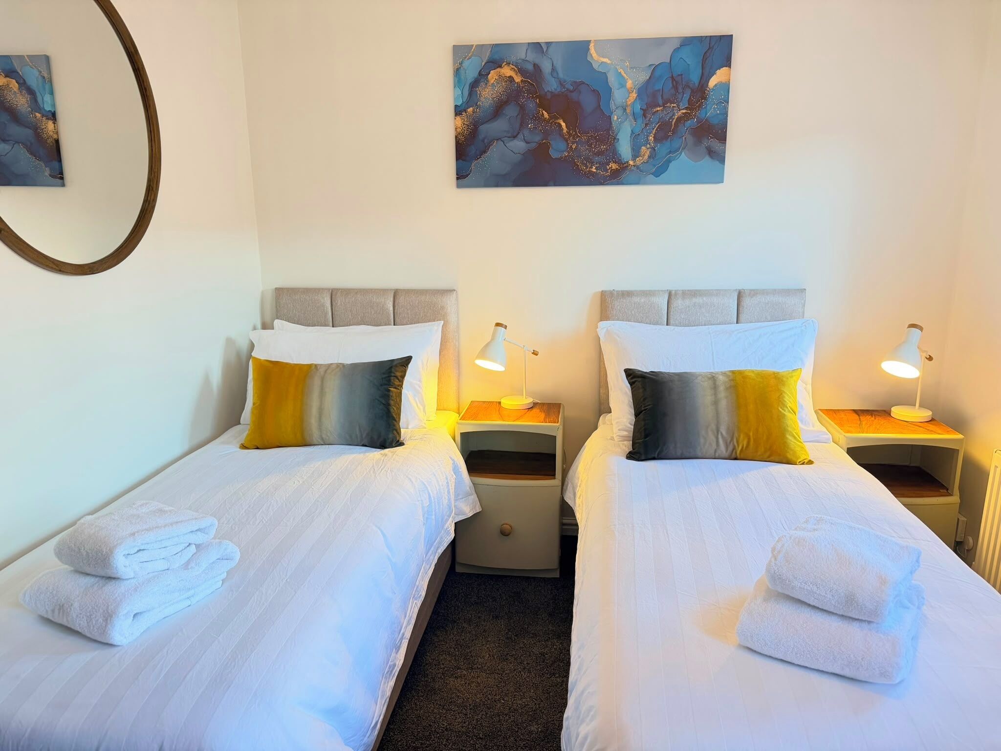 Une chambre d’hôtel avec deux lits, du linge de lit blanc et des oreillers assortis. Il y a des tables de chevet avec des lampes et un tableau au-dessus des lits.