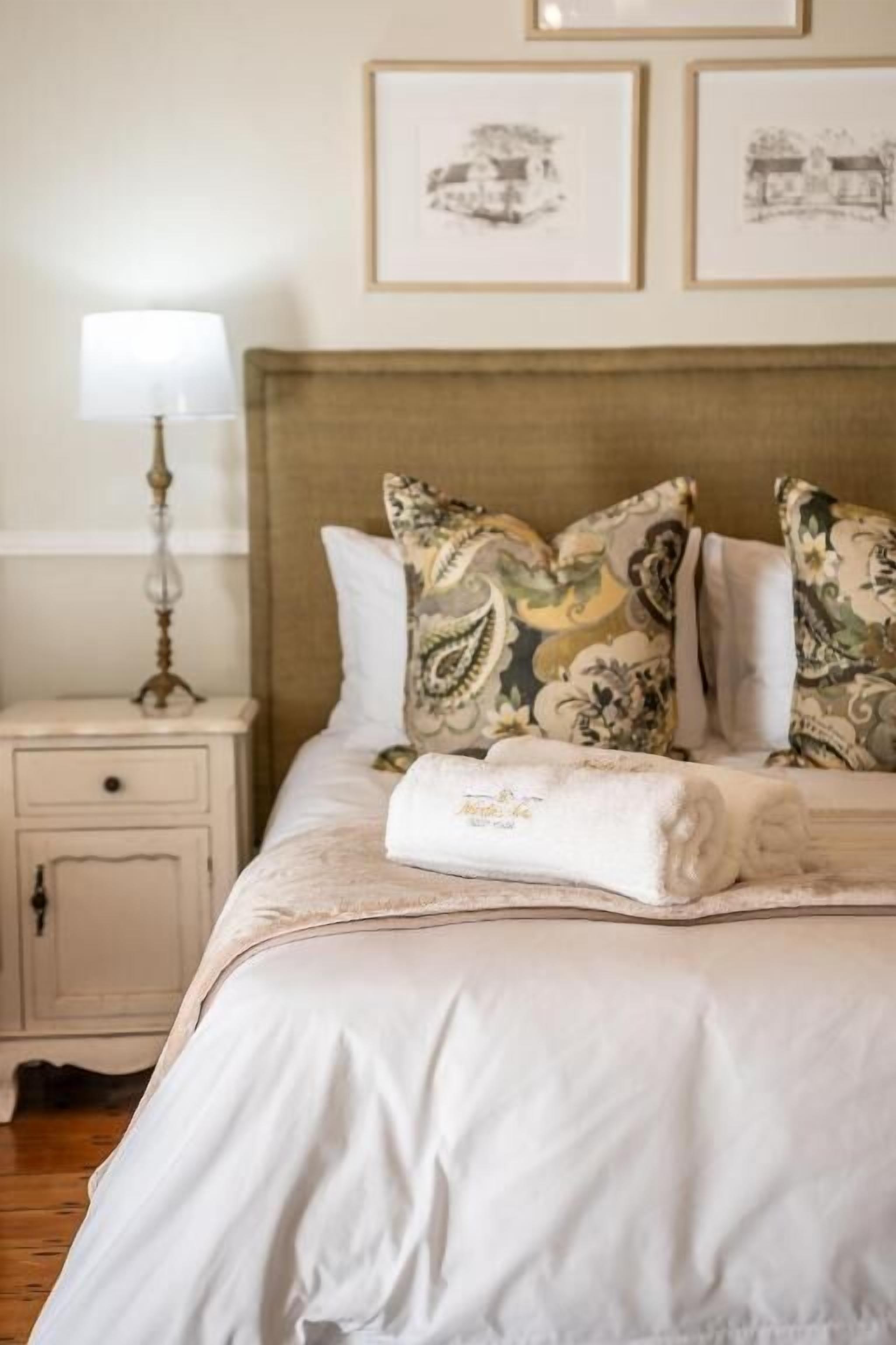A neatly made bed with patterned pillows, a bedside lamp, and framed artwork on the wall.