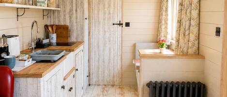 A compact kitchen with wooden cabinets, a red leather chair, a radiator, and a small trash bin.