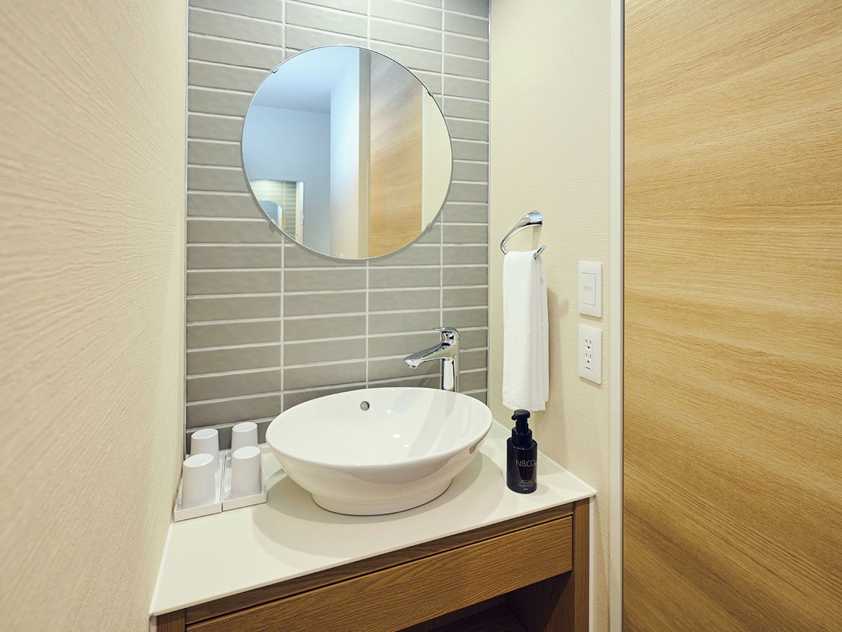 A bathroom with a round mirror, a white sink, and a wooden vanity.