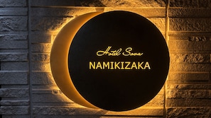 A circular sign with 'Hotel Sowa NAMIKIZAKA' text, mounted on a stone wall.