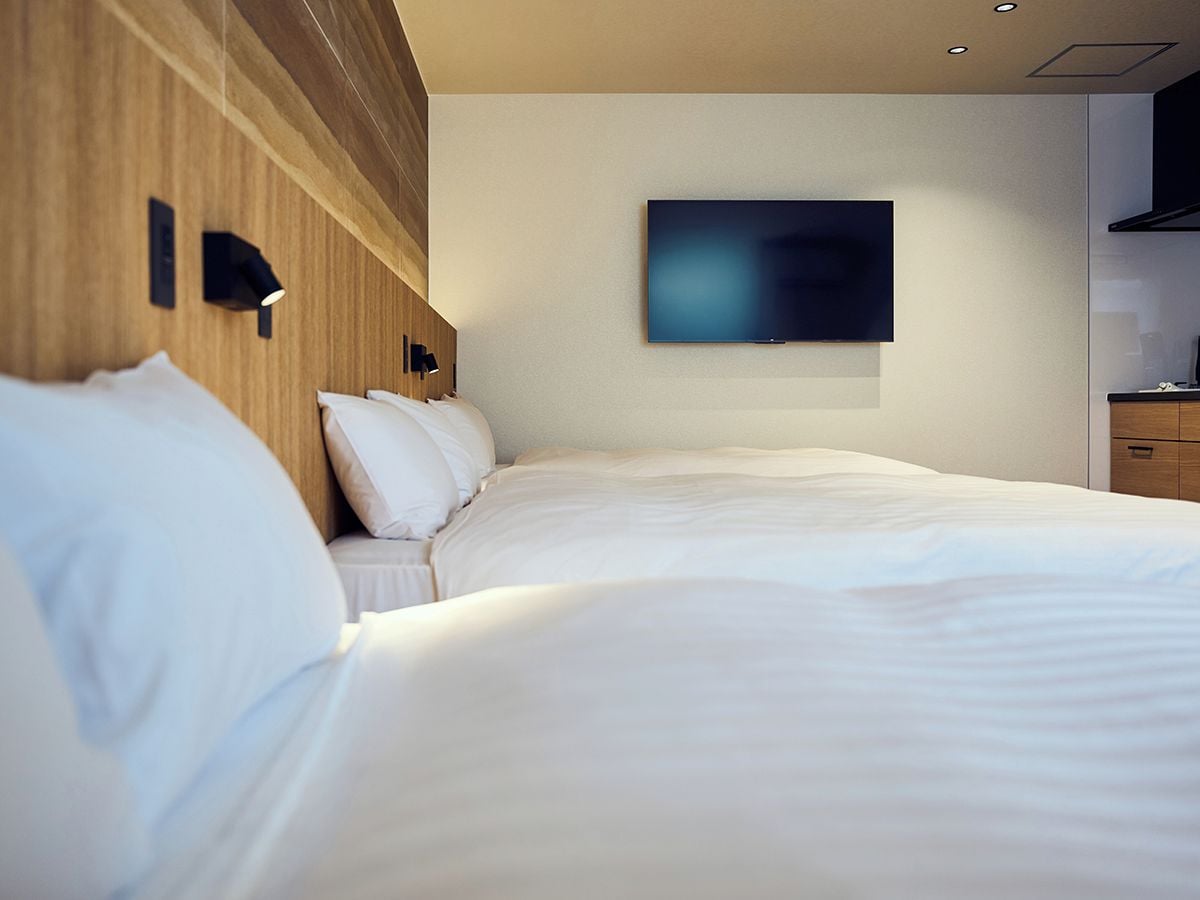 A hotel room with a bed, a flat-screen TV mounted on the wall, and a wooden headboard.
