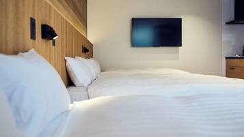 A hotel room with a bed, a flat-screen TV mounted on the wall, and a wooden headboard.