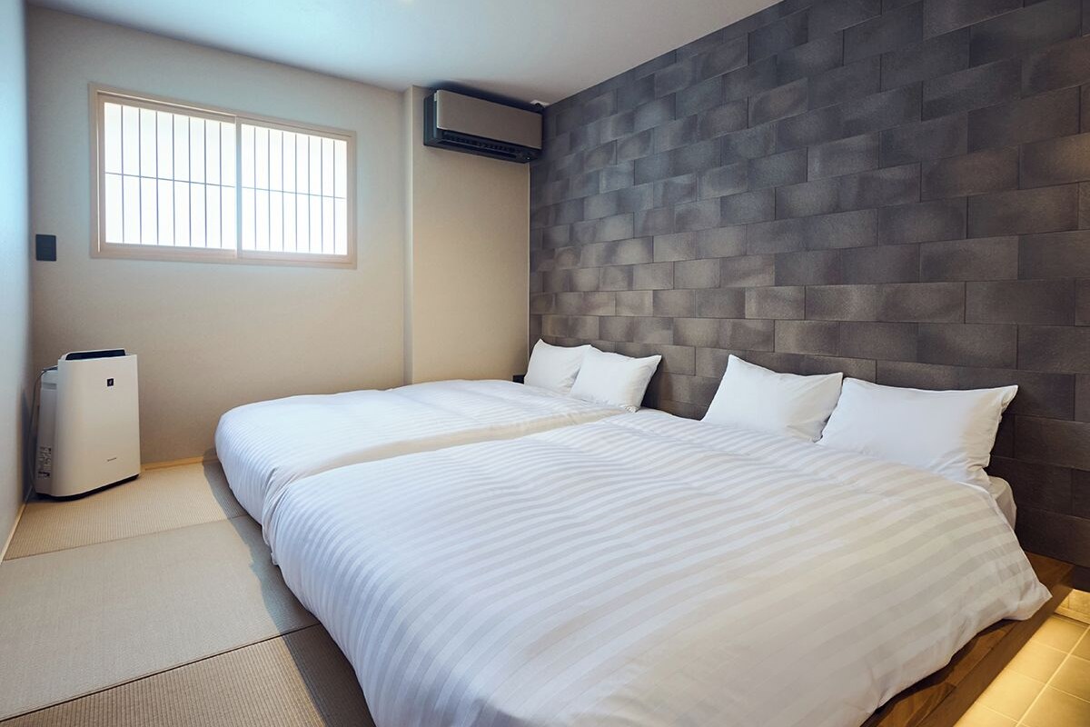 A hotel room with two beds, a large window, a wall-mounted air conditioner, and a portable heater.