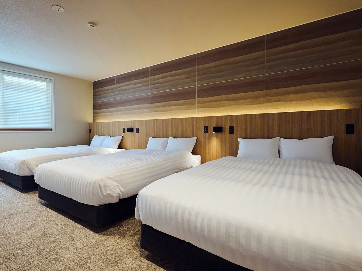 A hotel room with three beds, a large window, and a modern wooden headboard.