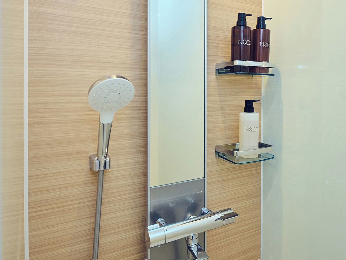 A bathroom with a shower, a mirror, and a shelf with toiletries.