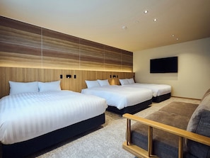 A hotel room with three beds, a flat-screen TV mounted on the wall, and a wooden headboard.