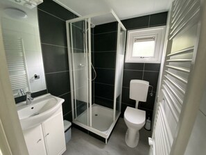 Ein Badezimmer mit Duschkabine, Toilette, Waschbecken und einem Fenster über der Toilette.