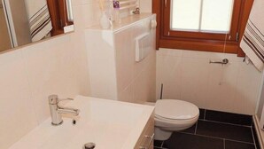 Une salle de bain avec un lavabo blanc, des toilettes et une fenêtre.