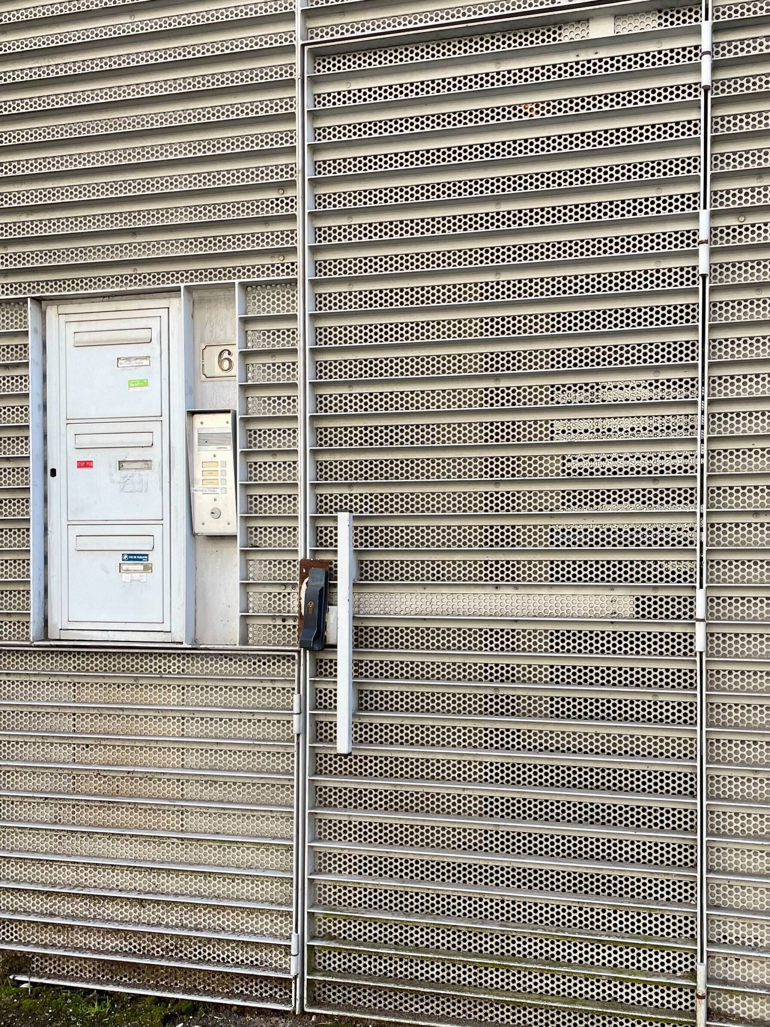 A metal facade with a series of horizontal slats and a utility box with a keypad.