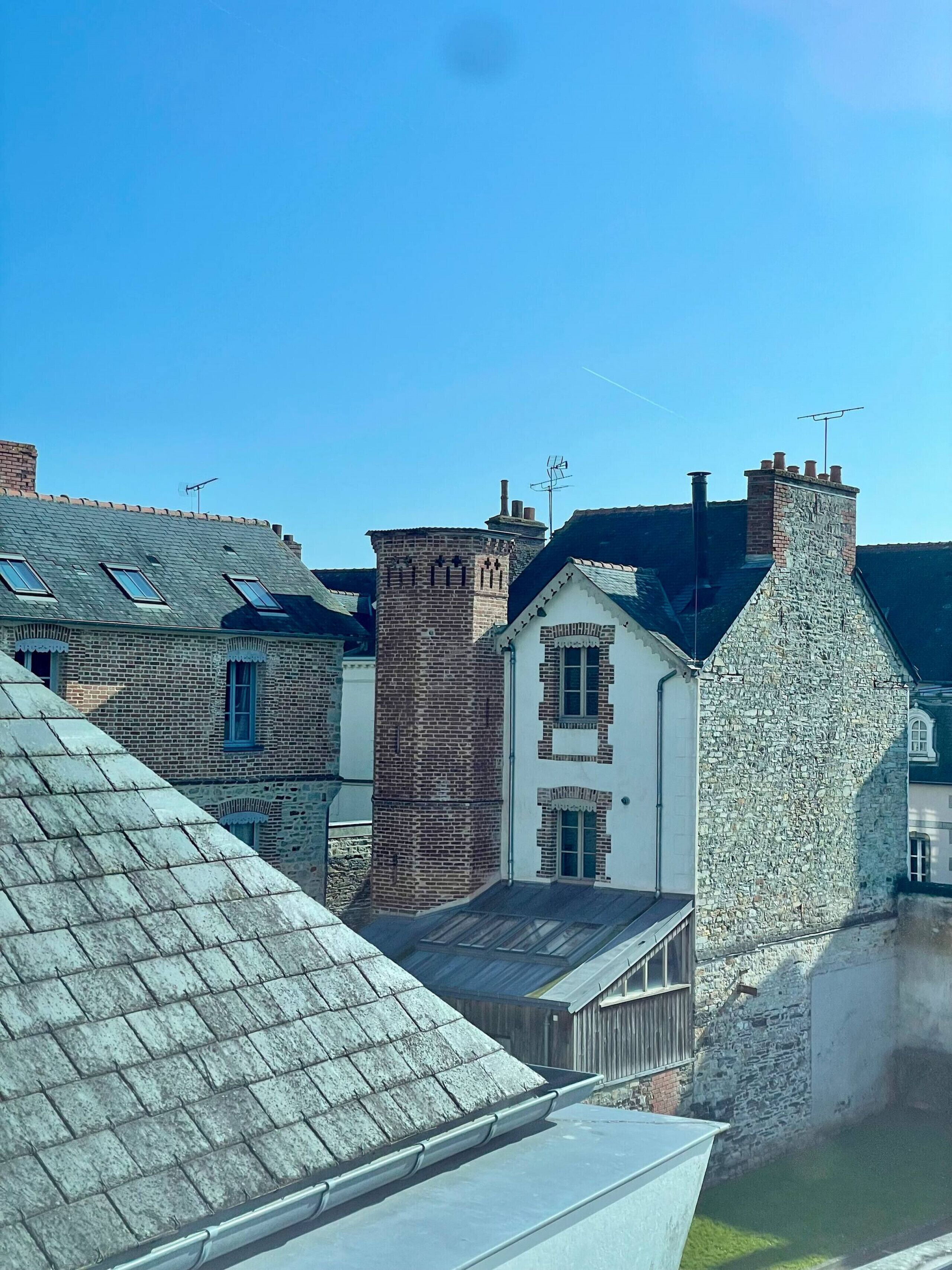 Un quartier résidentiel composé de plusieurs maisons, dont certaines ont des murs en pierre et d’autres des façades en briques, et qui se caractérisent par des toits à deux versants et des cheminées apparentes.