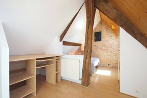 Een kamer met een schuine kap, houten balken, een radiator en een bed.