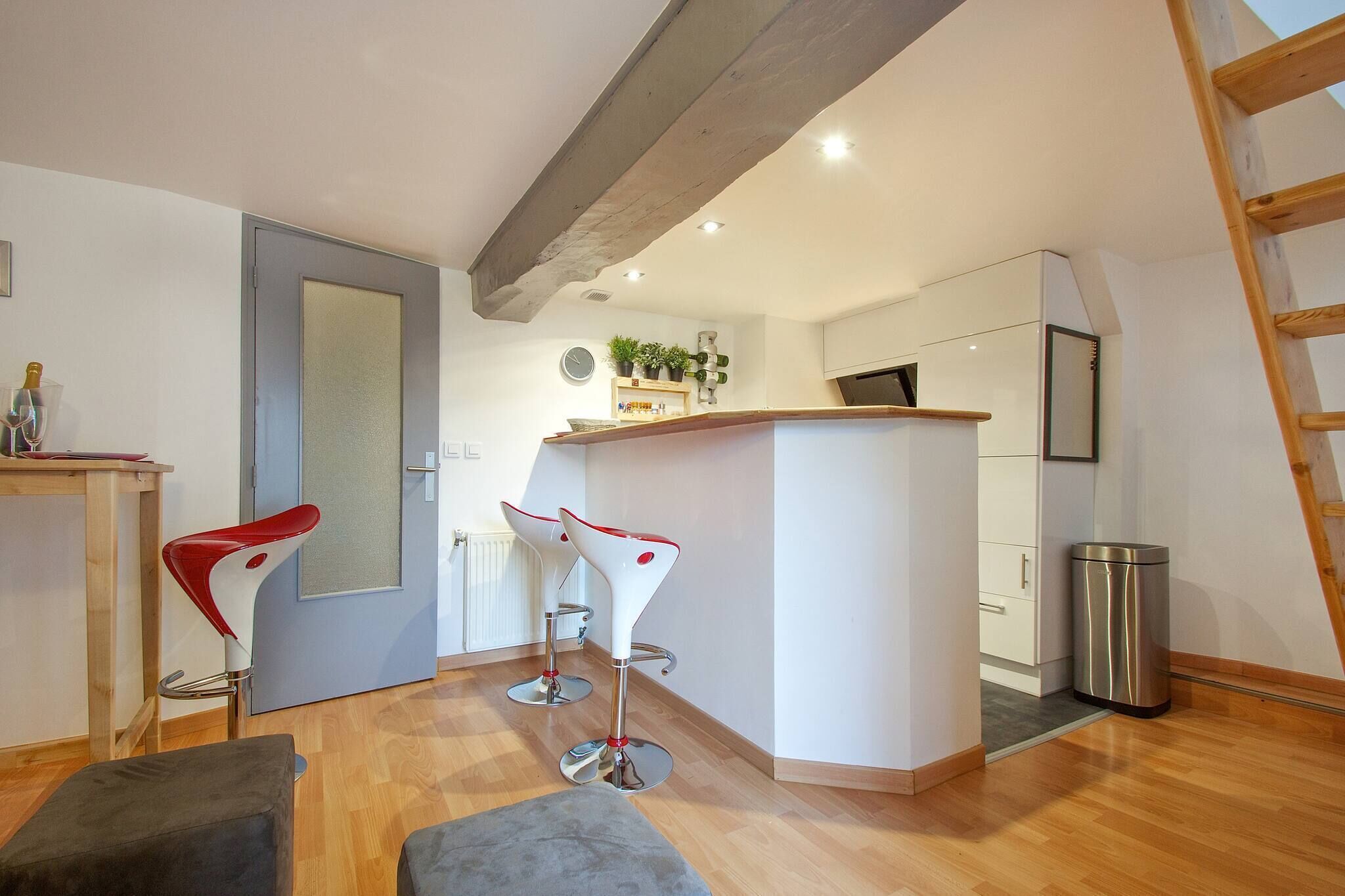 Een moderne keuken met een centraal eiland, twee barkrukken, een houten bank en een prullenbak.