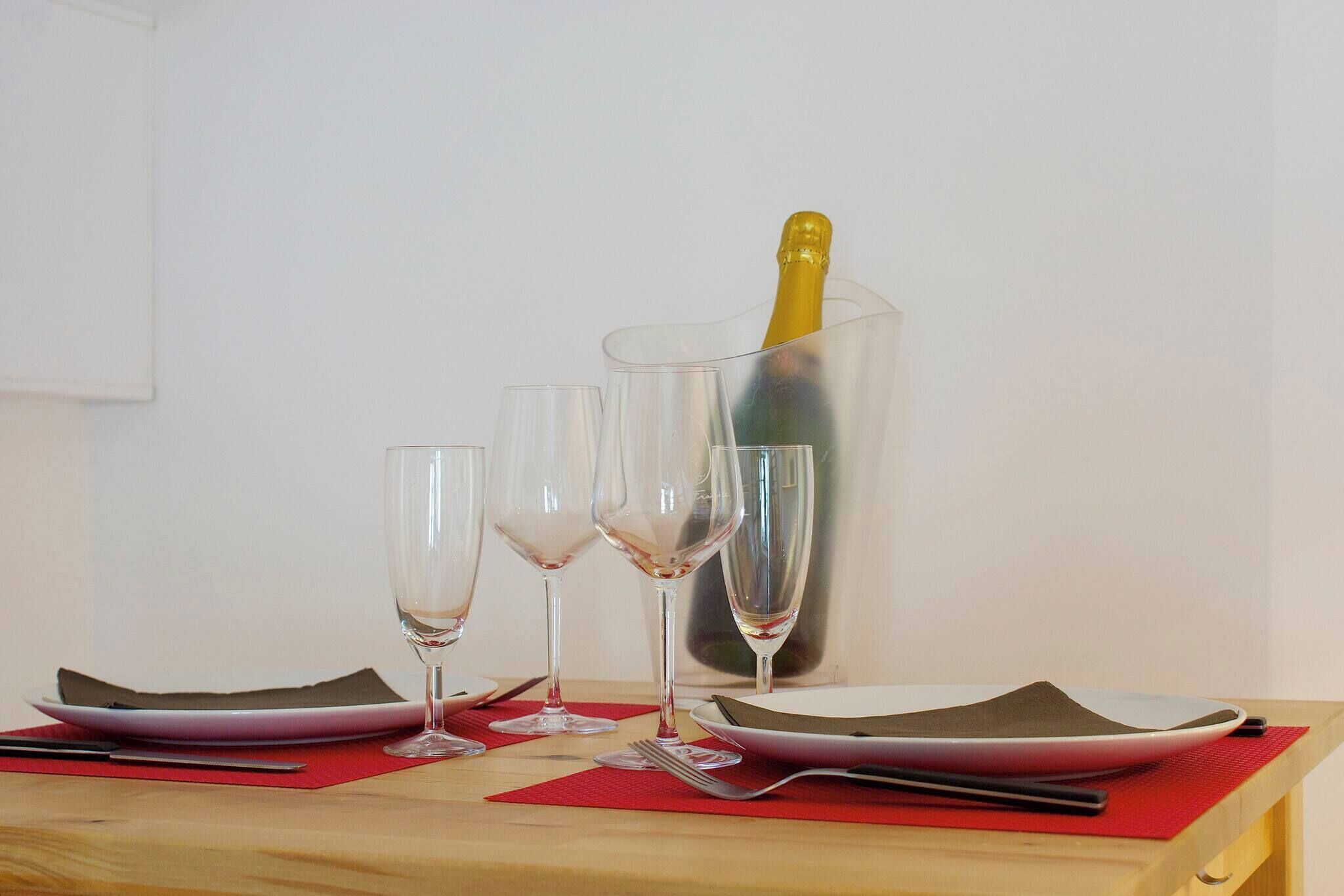 Una mesa con tres copas de vino, una botella de champán en un cubo de hielo transparente y un mantel individual rojo.