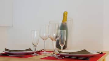 Una mesa con tres copas de vino, una botella de champán en un cubo de hielo transparente y un mantel individual rojo.