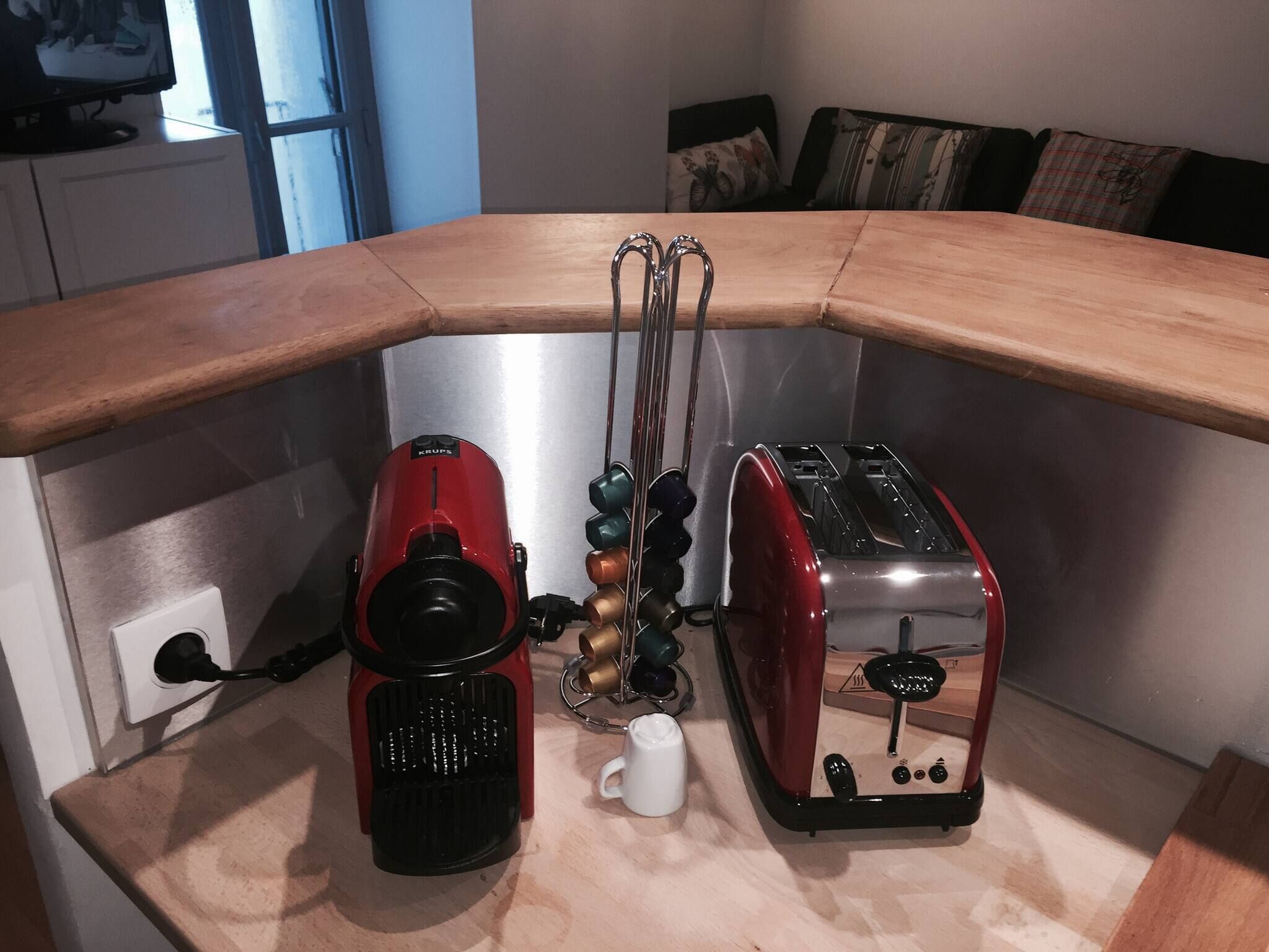 Una cocina con encimera de madera, una cafetera roja, un tostador y una taza blanca.