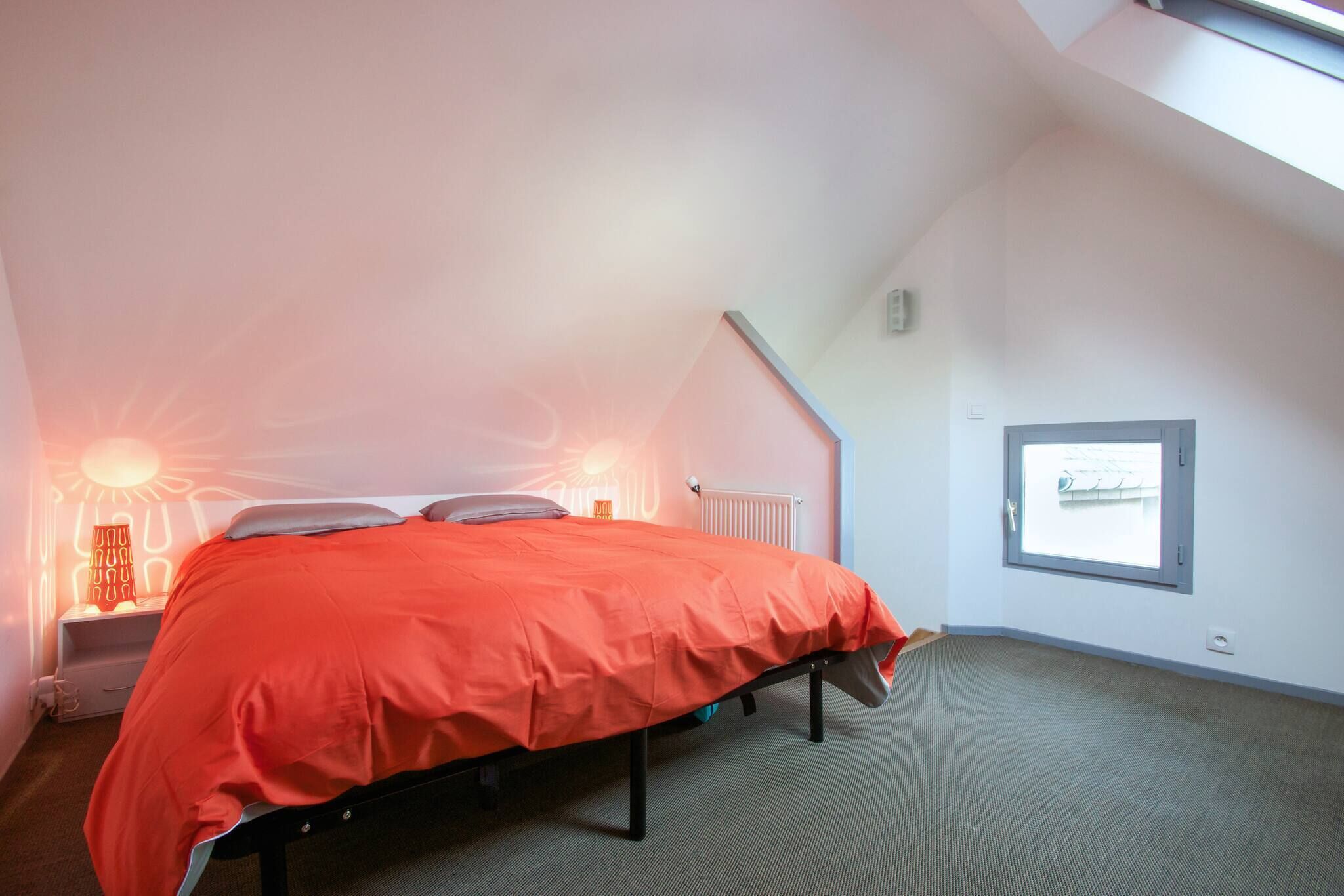 Quarto com cama, mesa de cabeceira, luminária, janela e radiador.