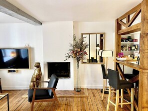 A living room with a TV, a decorative bear statue, a vase with dried flowers, a mirror, and a wooden bookshelf. - AppartCosy 01 faubourg Rachapt T2 (Vitré)