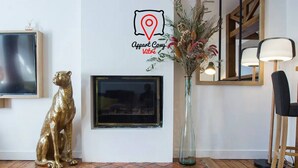 A room with a framed television, a decorative golden statue, a vase with dried flowers, and a mirror.