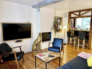 Een woonkamer met een televisie, een bank, een salontafel en een open haard.