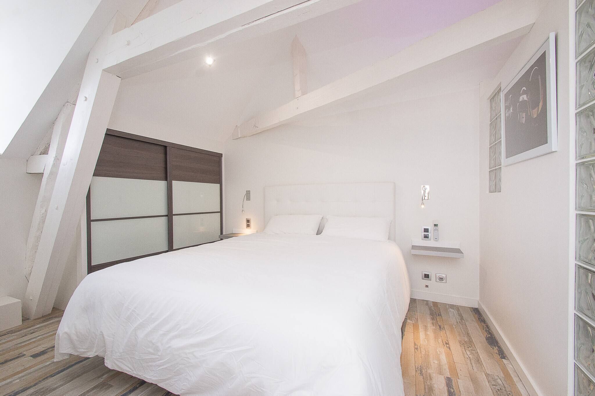 Ein Schlafzimmer mit einem großen Bett, einem Nachttisch, einer Ablage und einem Fenster mit Jalousien.