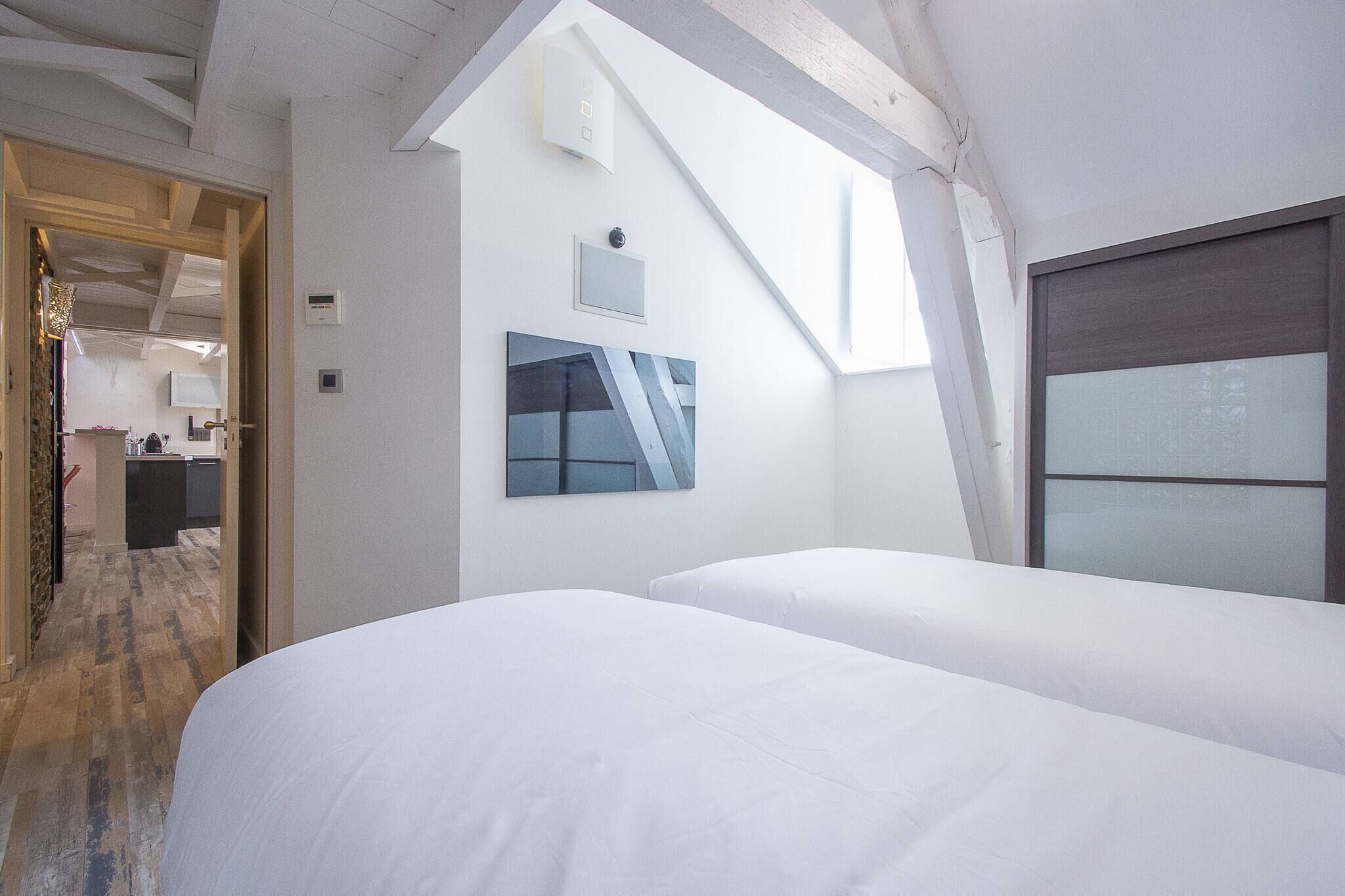 A modern hotel room with a sloped ceiling, a large window, and a painting on the wall.