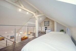 Een slaapkamer met een groot bed, een bureau en een stoel, een trap en uitzicht op de verdieping beneden.