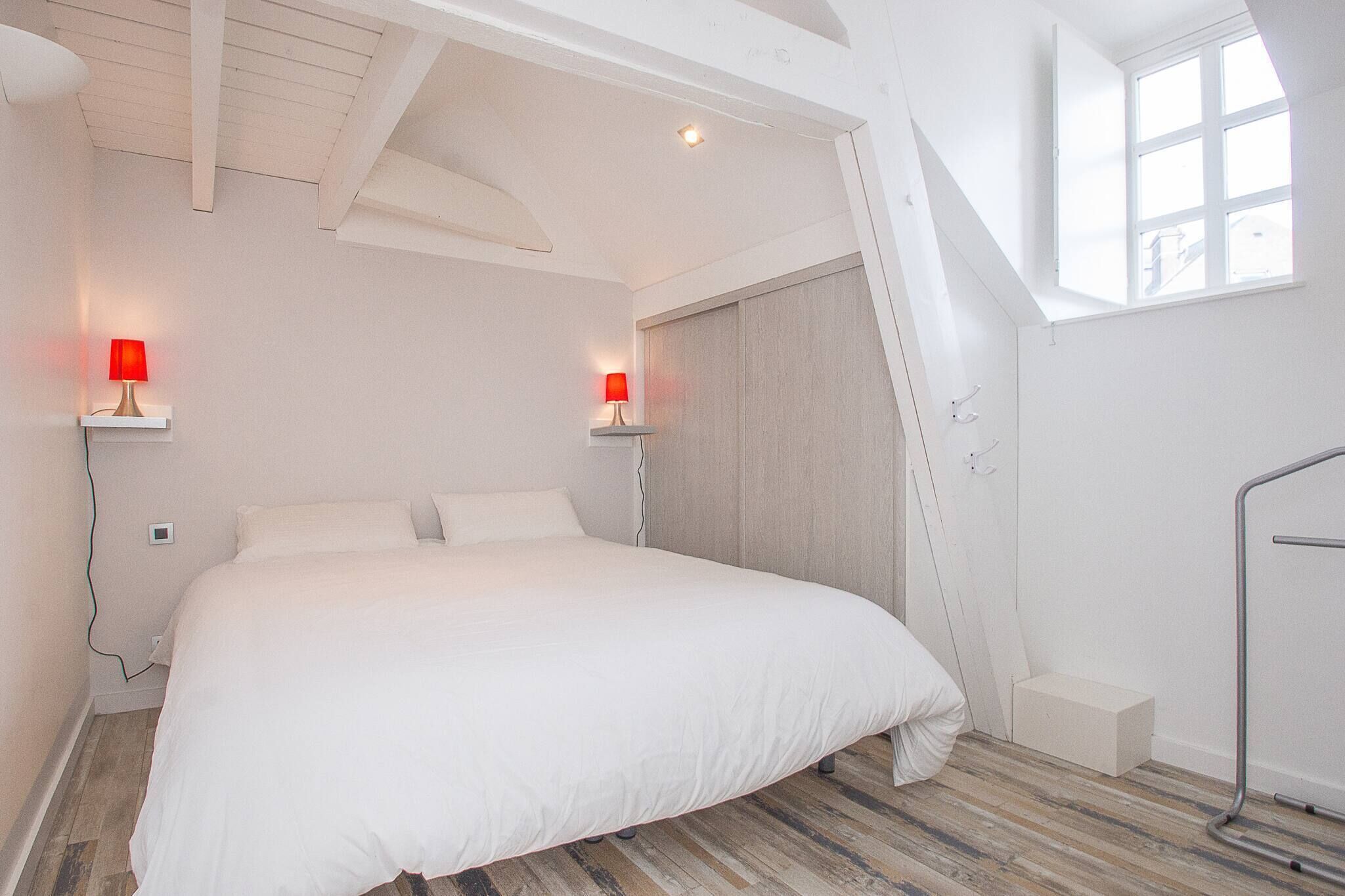 A bedroom with a bed, two bedside lamps, a window, and a skylight.