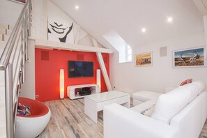 Een moderne woonkamer met een flatscreen televisie, witte banken, een rode accentmuur en een trap.