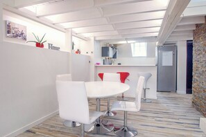 Een modern interieur met een witte eettafel, witte stoelen, een rode accentstoel, een keuken en een bakstenen muur.
