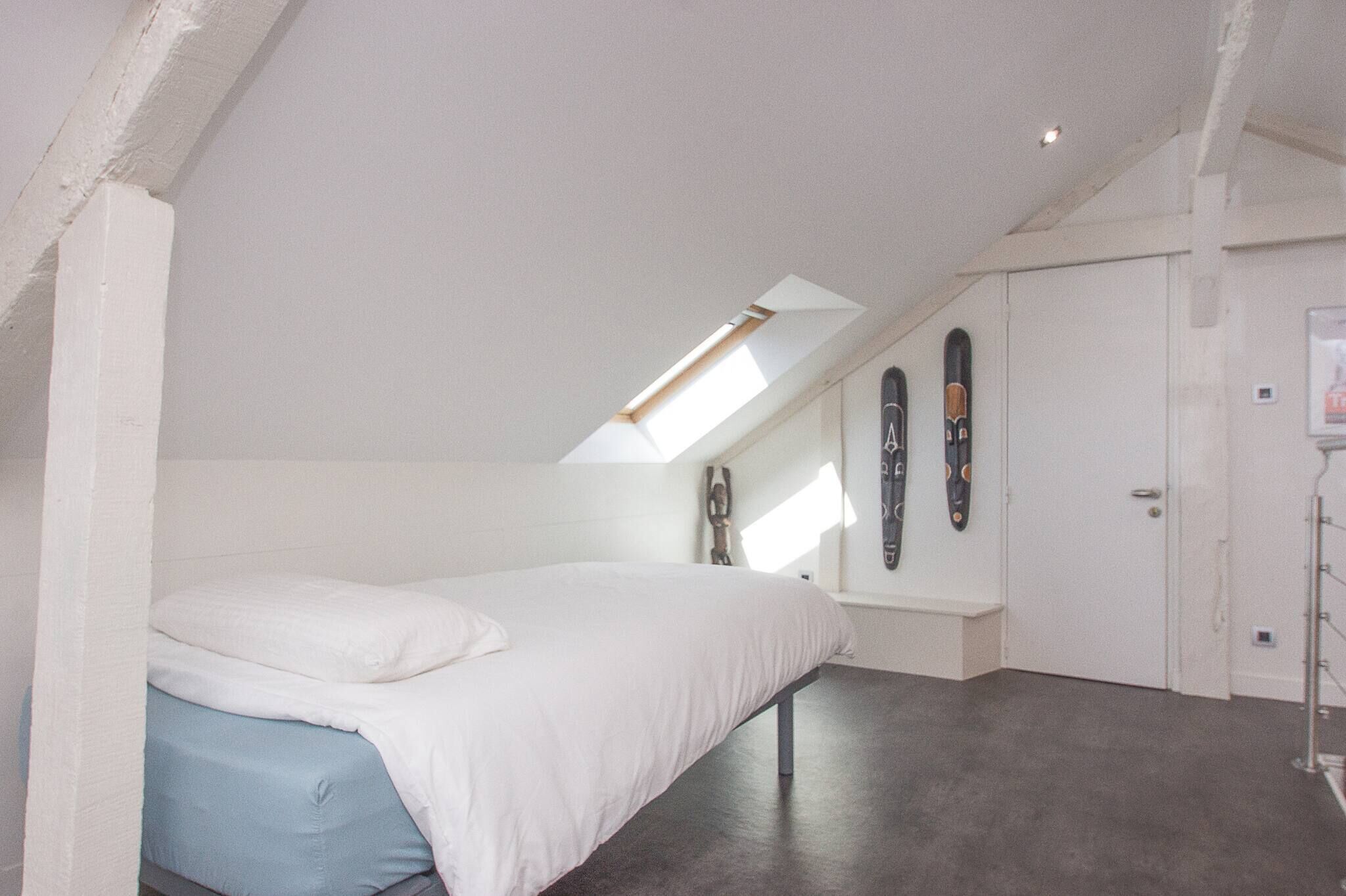 A bedroom with a sloped ceiling, a bed, a small window, and a door.