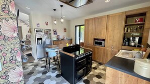 A modern kitchen with a central island, wooden cabinets, a microwave, and a refrigerator. - Riverside House with Jacuzzi (Vitré)