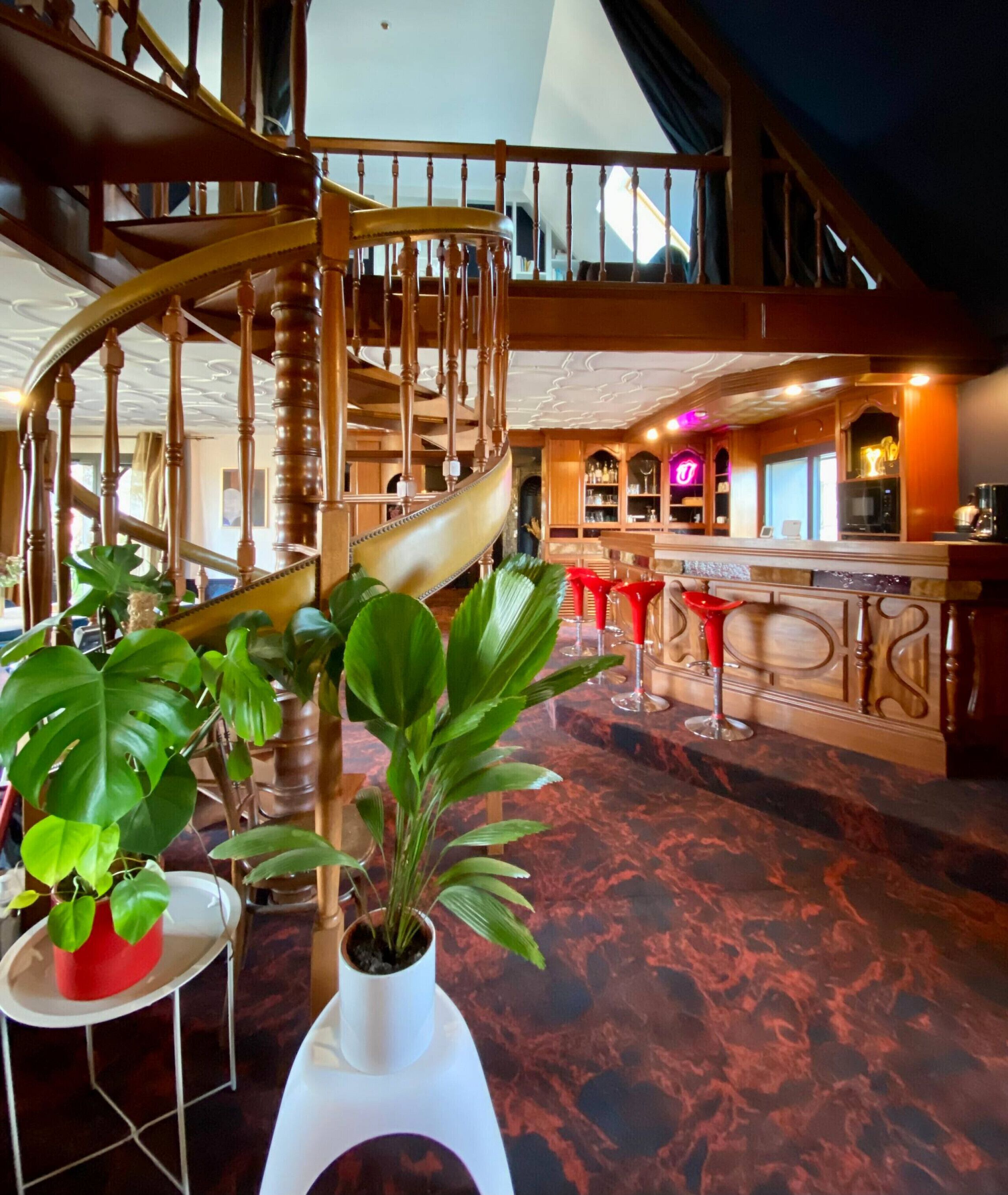 Um interior espaçoso com uma escadaria imponente, área de bar e plantas em vasos.