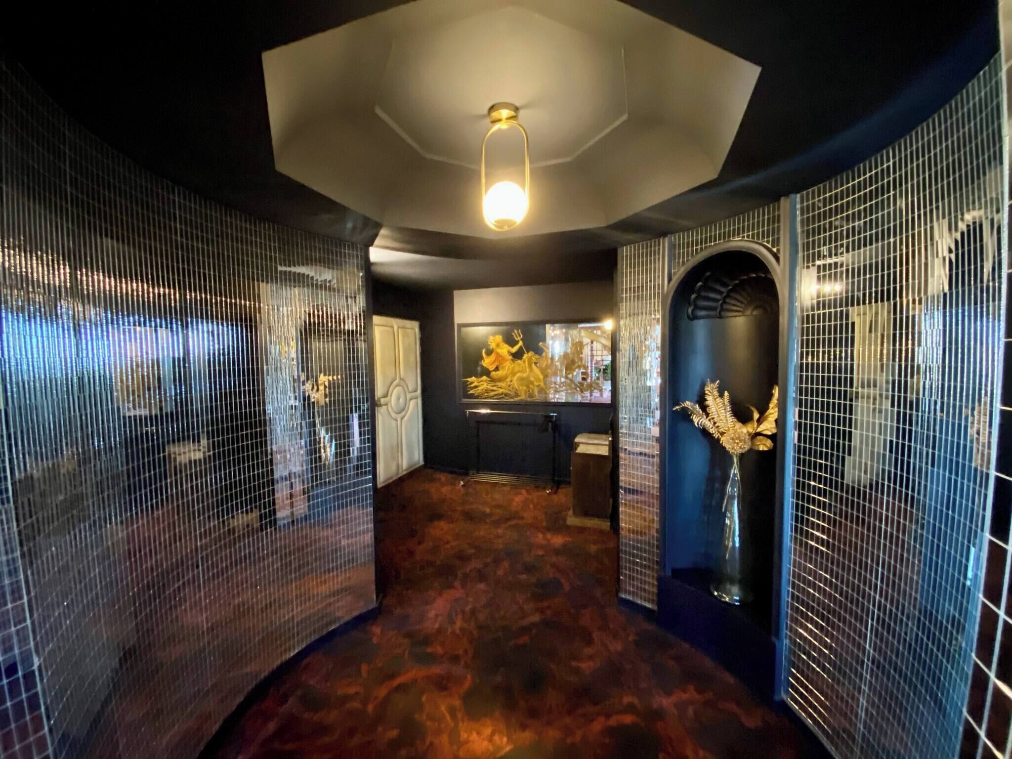 Een gang met spiegelende wanden, een plafondlamp en een decoratief gouden beeld.