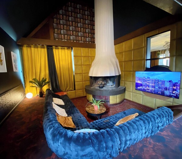 A cozy living room with a blue sofa, a fireplace, a television, and a bookshelf. - AppartCosy 15 ArtDéco (Vitré)
