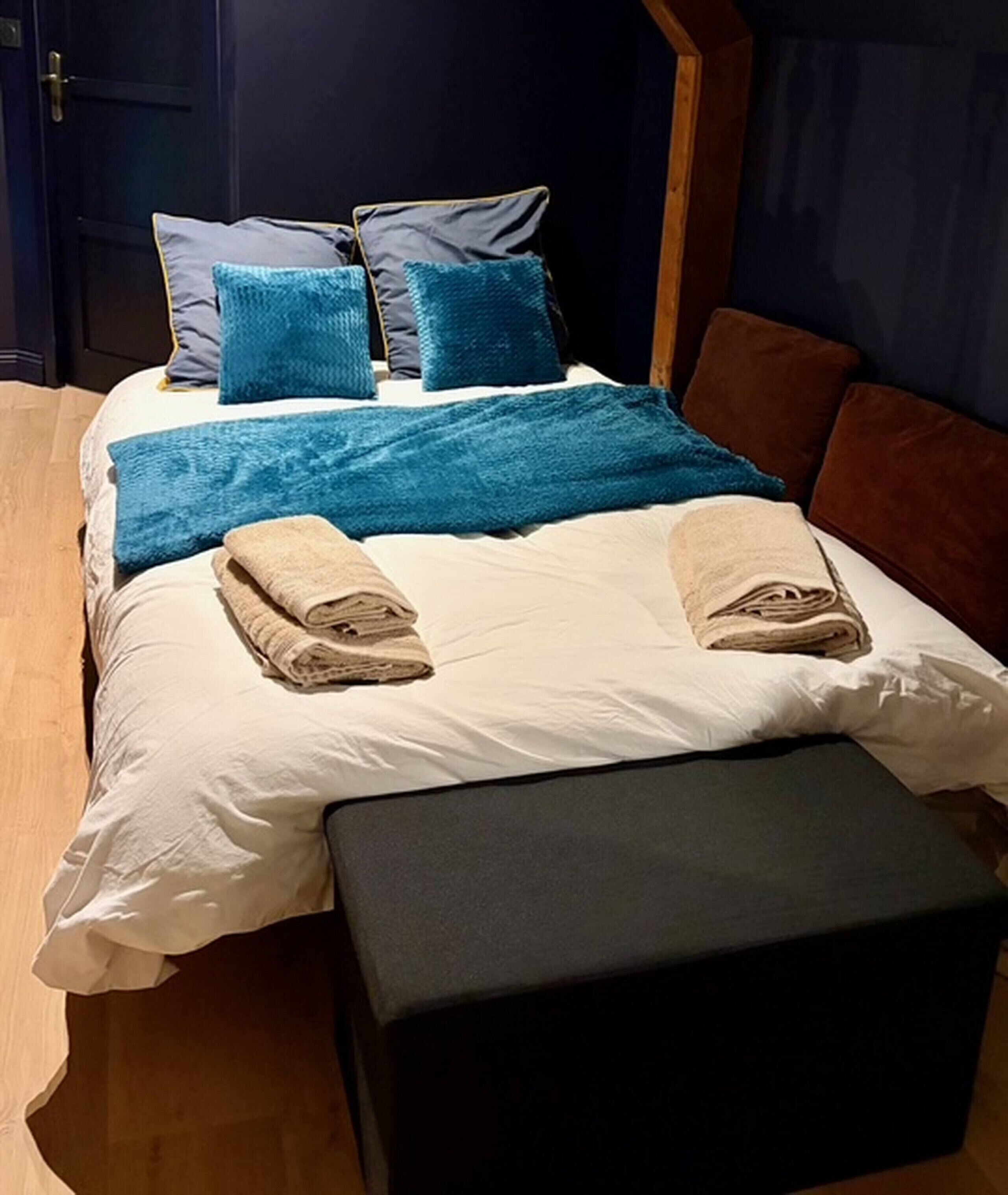 Un lit avec des oreillers bleus, une couverture bleue et deux serviettes pliées.