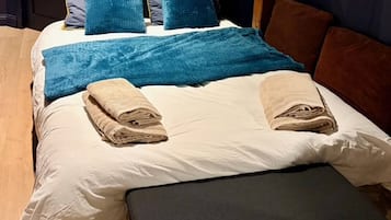 Een bed met blauwe kussens, een blauwe deken en twee opgevouwen handdoeken.