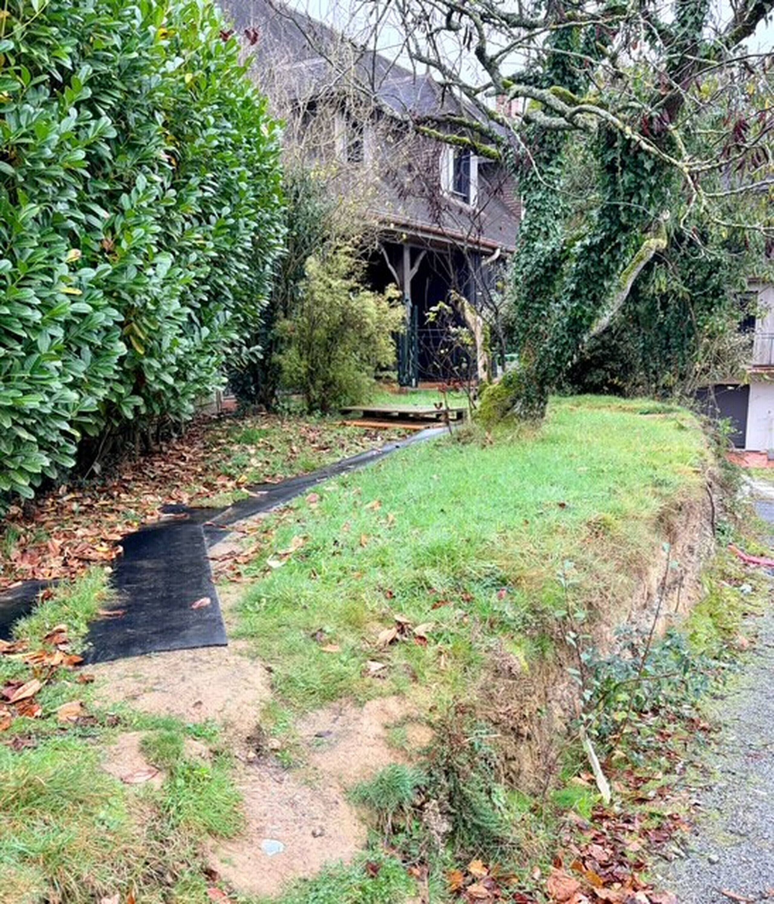 Een woonhuis met een pad dat naar de voordeur leidt, omringd door weelderige beplanting en een klein terras.