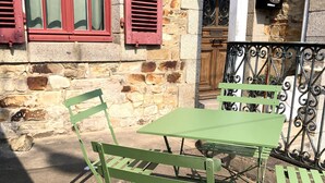A stone building with a red window shutter, a metal gate, and a green metal table and chair set. - AppartCosy 09 for 4 people in a charming house (Vitré)