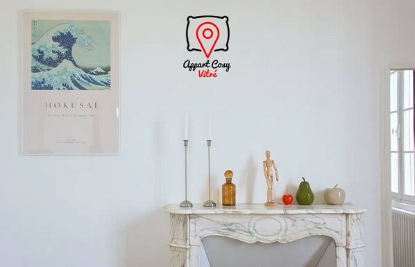 Ein Zimmer mit Kamin aus weißem Marmor, einem gerahmten Kunstwerk von Hokusais 'Die große Welle vor Kanagawa' und einem Schild mit der Aufschrift 'Apart Cosy Kitré'.