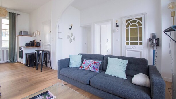 A living room with a grey sofa, a glass coffee table, and a kitchen area with appliances and a dining table. - AppartCosy 09 for 4 people in a charming house (Vitré)