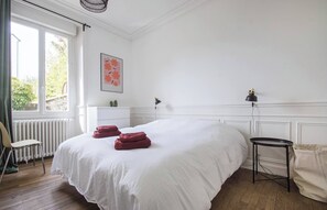 Ein Schlafzimmer mit einem großen Bett, einem Sessel, einem kleinen Tisch, einem Heizkörper und einem Fenster.