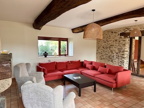 A living room with a red sectional sofa, a grey armchair, a black coffee table, a wicker pendant light, and a stone wall.