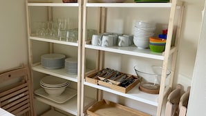A kitchen with white shelves holding plates, bowls, glasses, and utensils.
