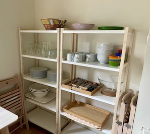 Une cuisine avec des étagères blanches où sont rangées des assiettes, des bols, des verres et des ustensiles.